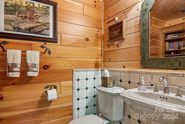 bathroom featuring toilet, sink, and wooden walls