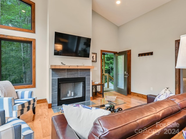 living room featuring light wood-type flooring, a tile fireplace, and high vaulted ceiling