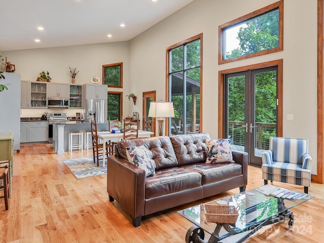 living room with light wood-type flooring, a healthy amount of sunlight, french doors, and high vaulted ceiling