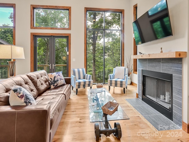 living room with plenty of natural light, a tile fireplace, french doors, and light hardwood / wood-style flooring