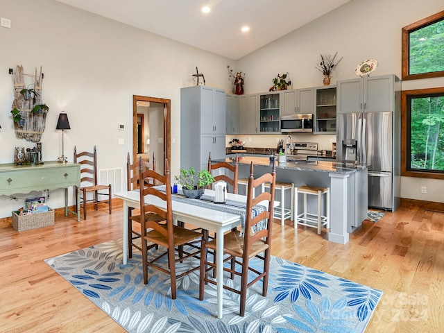 dining room featuring high vaulted ceiling, sink, and light hardwood / wood-style floors