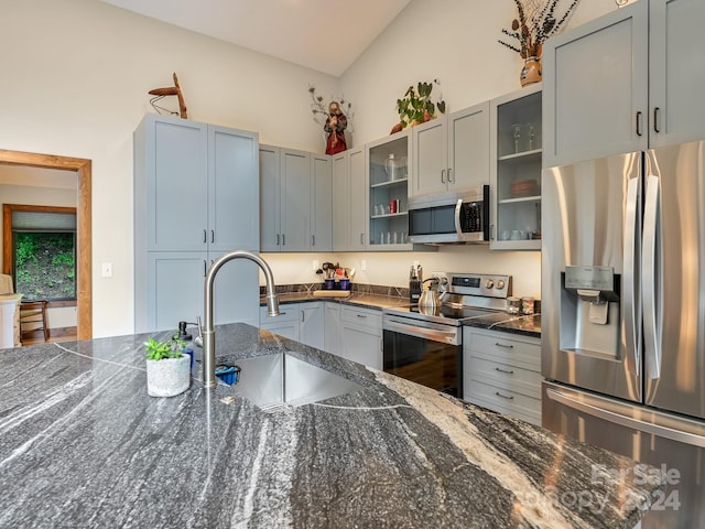 kitchen featuring gray cabinets, stainless steel appliances, dark stone countertops, vaulted ceiling, and sink