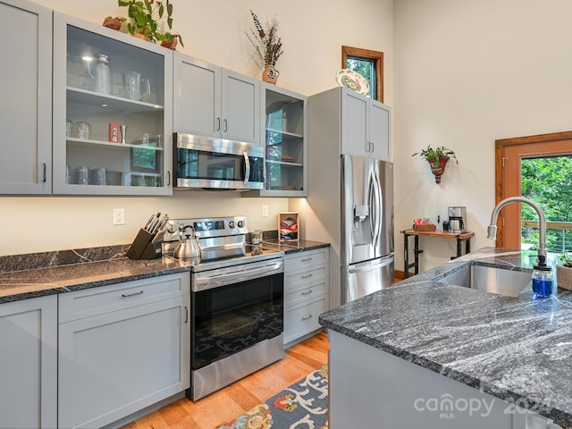 kitchen featuring appliances with stainless steel finishes, dark stone countertops, sink, gray cabinets, and light wood-type flooring