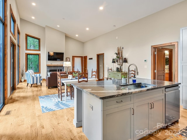 kitchen featuring a tiled fireplace, a kitchen island with sink, stone counters, light hardwood / wood-style flooring, and sink