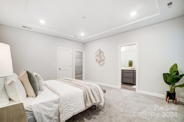 carpeted bedroom with a tray ceiling and ensuite bathroom