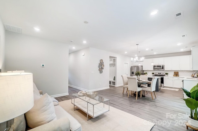 living room with an inviting chandelier, sink, and light hardwood / wood-style floors