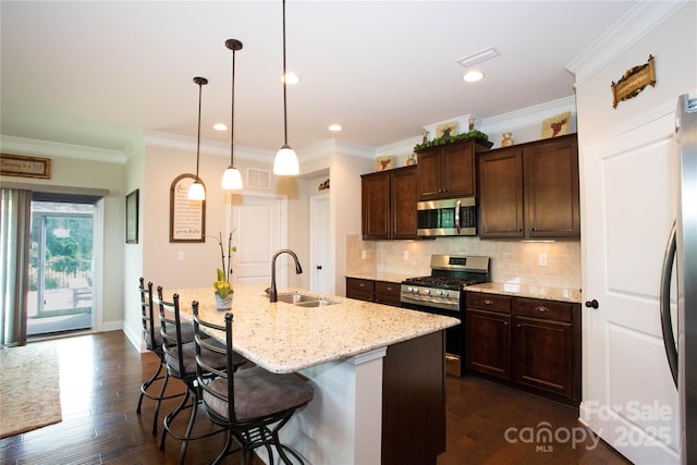 kitchen featuring a breakfast bar, a kitchen island with sink, sink, appliances with stainless steel finishes, and decorative light fixtures