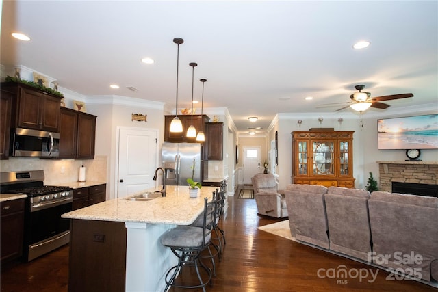 kitchen featuring appliances with stainless steel finishes, a kitchen island with sink, sink, a stone fireplace, and a breakfast bar area