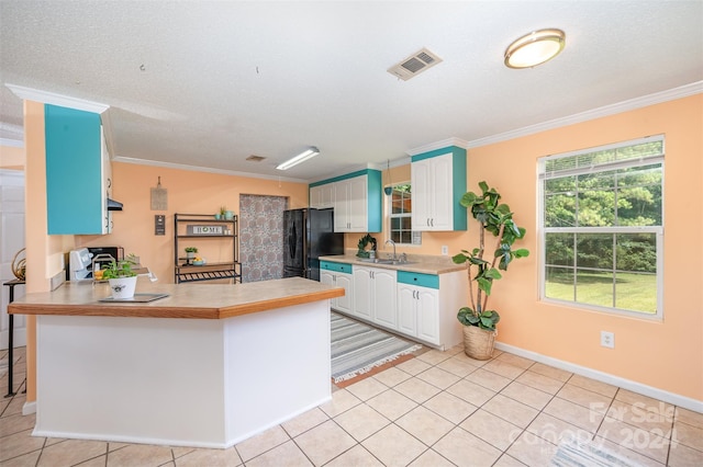 kitchen with white cabinetry, kitchen peninsula, black fridge, and crown molding