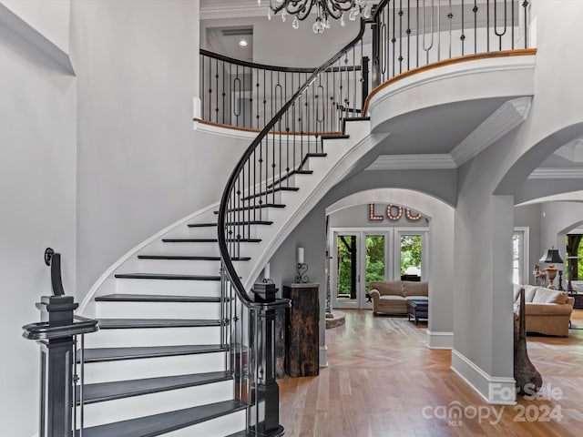 foyer entrance featuring crown molding, a towering ceiling, hardwood / wood-style floors, and a notable chandelier