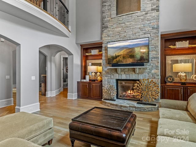 living room with light hardwood / wood-style floors, a high ceiling, and a stone fireplace