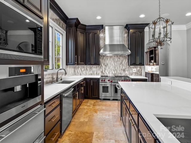 kitchen featuring pendant lighting, appliances with stainless steel finishes, wall chimney exhaust hood, tasteful backsplash, and sink