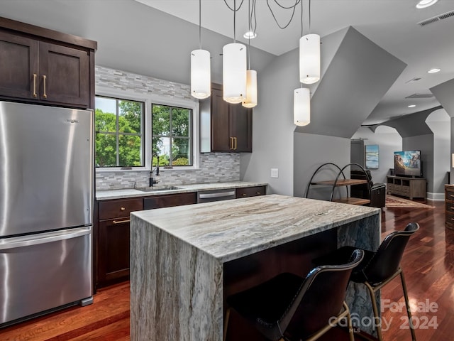 kitchen featuring decorative light fixtures, a kitchen island, a kitchen bar, sink, and stainless steel appliances