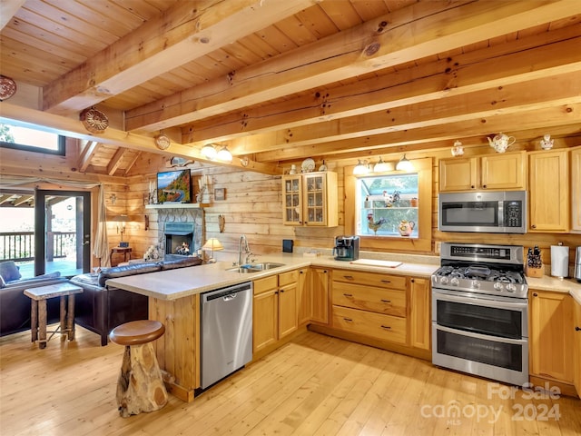 kitchen featuring wood walls, stainless steel appliances, light hardwood / wood-style flooring, beam ceiling, and a fireplace