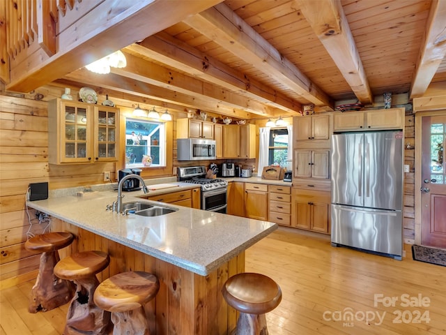 kitchen with appliances with stainless steel finishes, light wood-style floors, glass insert cabinets, a sink, and a peninsula