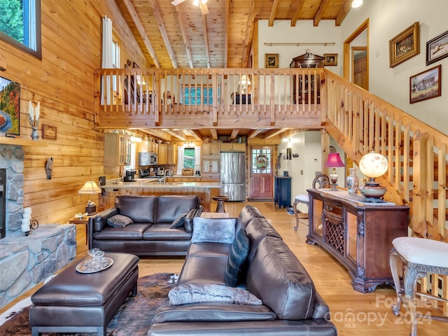 living room with light hardwood / wood-style floors, high vaulted ceiling, a stone fireplace, and wooden walls