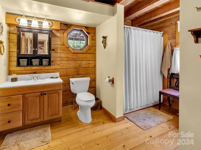 bathroom with wooden walls, toilet, hardwood / wood-style flooring, vanity, and beam ceiling