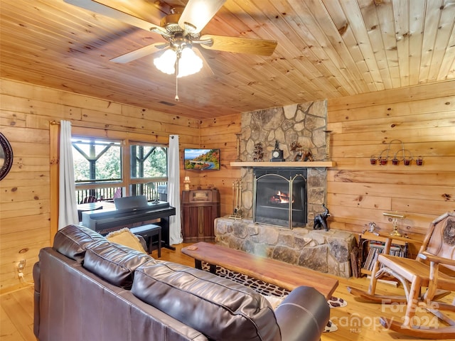 living room featuring hardwood / wood-style floors, a stone fireplace, wooden ceiling, wooden walls, and ceiling fan