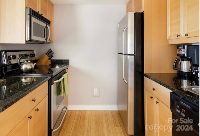 kitchen featuring stainless steel appliances, dark stone countertops, light hardwood / wood-style floors, and light brown cabinets