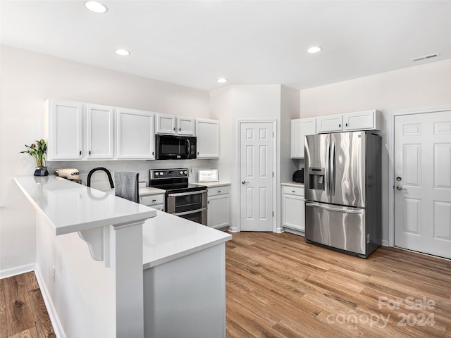 kitchen featuring white cabinets, appliances with stainless steel finishes, kitchen peninsula, and light wood-type flooring