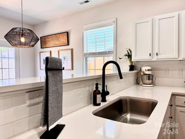 kitchen with a wealth of natural light, decorative light fixtures, white cabinets, and sink