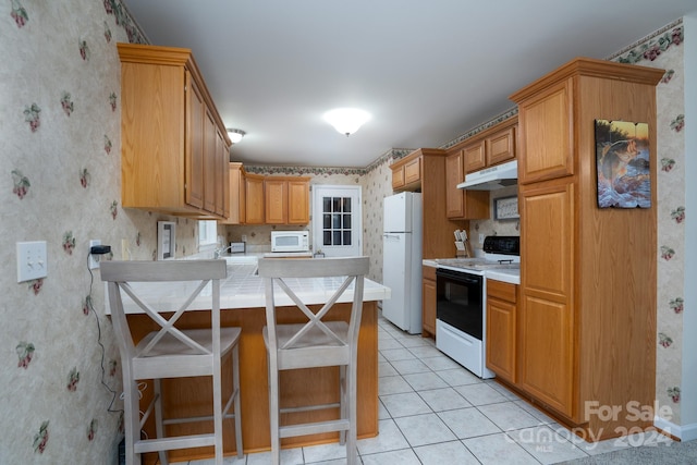 kitchen with a kitchen bar, light tile patterned floors, white appliances, and kitchen peninsula