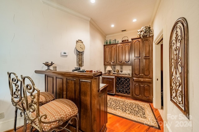 bar featuring light hardwood / wood-style floors, ornamental molding, and dark brown cabinetry