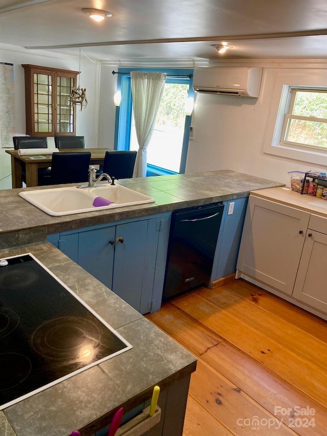 kitchen featuring pendant lighting, black appliances, sink, a wall mounted AC, and light hardwood / wood-style flooring