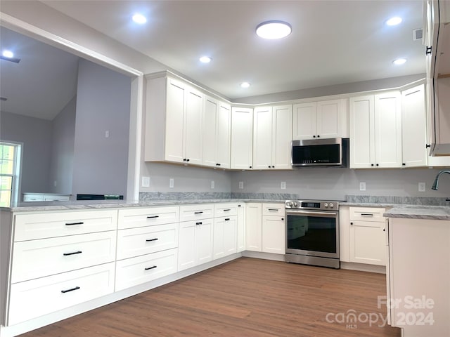 kitchen with kitchen peninsula, appliances with stainless steel finishes, light stone counters, white cabinets, and dark hardwood / wood-style floors