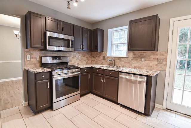 kitchen with backsplash, sink, dark brown cabinetry, light stone countertops, and stainless steel appliances