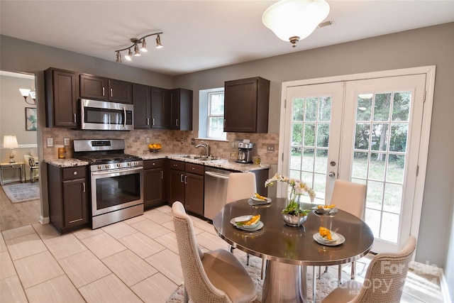 kitchen with stainless steel appliances, tasteful backsplash, dark brown cabinets, light stone countertops, and sink