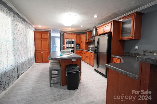 kitchen featuring appliances with stainless steel finishes, a kitchen island with sink, a kitchen breakfast bar, wall chimney range hood, and ornamental molding