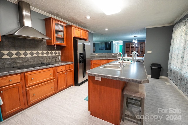 kitchen featuring sink, stainless steel fridge with ice dispenser, a kitchen island with sink, wall chimney range hood, and black electric cooktop