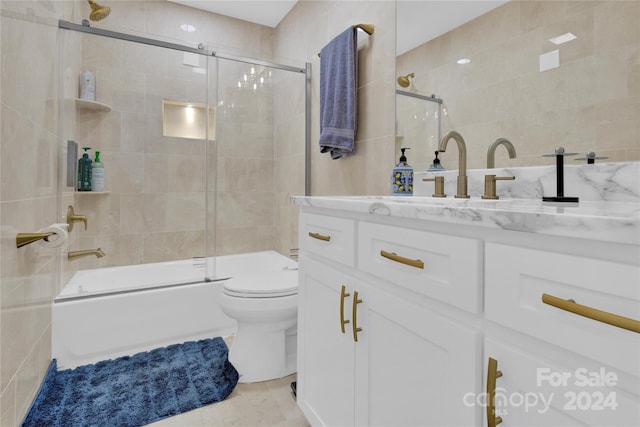 full bathroom with toilet, vanity, tile walls, and bath / shower combo with glass door