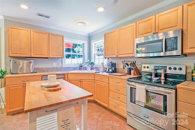 kitchen featuring light tile patterned flooring, light brown cabinetry, appliances with stainless steel finishes, and butcher block counters