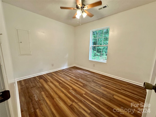 empty room featuring ceiling fan, electric panel, and dark hardwood / wood-style floors