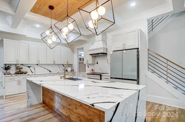 kitchen featuring custom exhaust hood, light hardwood / wood-style flooring, stainless steel fridge, decorative light fixtures, and white cabinetry