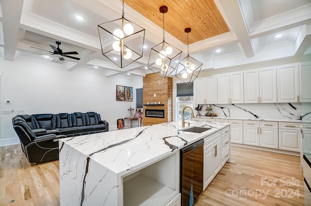 kitchen featuring light stone counters, a center island with sink, decorative light fixtures, and light wood-type flooring