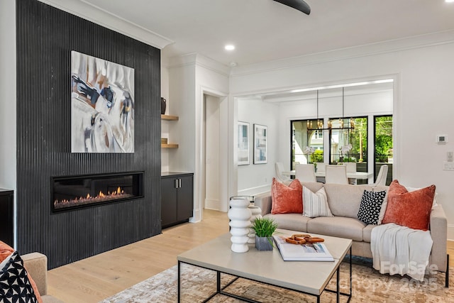 living area featuring light wood-style floors, a glass covered fireplace, recessed lighting, baseboards, and ornamental molding