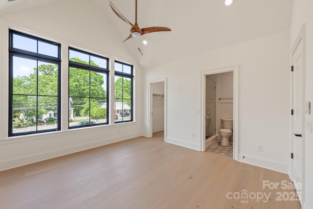 unfurnished bedroom with baseboards, a walk in closet, high vaulted ceiling, and light wood-style floors