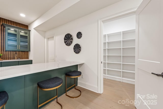 kitchen with a kitchen breakfast bar, baseboards, green cabinetry, and light wood-style floors