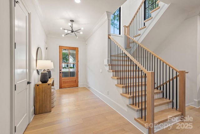 entrance foyer with ornamental molding, wood finished floors, a chandelier, and stairway