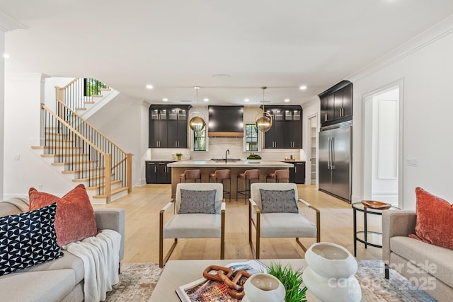 living room featuring recessed lighting, light wood finished floors, crown molding, and stairway