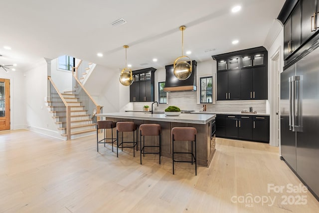 kitchen featuring dark cabinets, backsplash, custom exhaust hood, and built in fridge