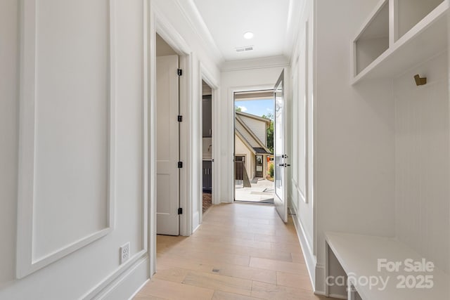 corridor featuring crown molding, light wood-style floors, and visible vents