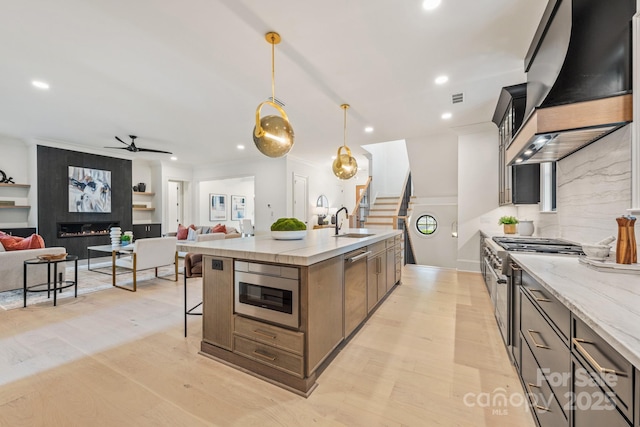 kitchen featuring appliances with stainless steel finishes, a sink, a breakfast bar area, premium range hood, and open floor plan