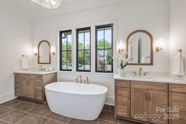 full bath with baseboards, a freestanding bath, two vanities, and a sink