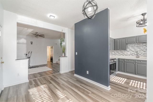 interior space with stainless steel range with electric stovetop, backsplash, sink, hanging light fixtures, and gray cabinets