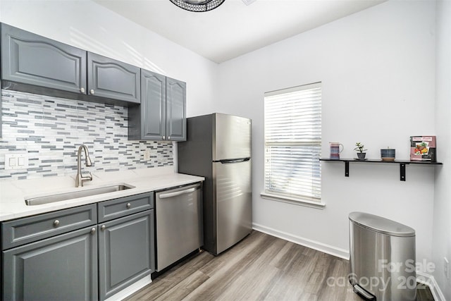 kitchen with gray cabinetry, sink, backsplash, appliances with stainless steel finishes, and light wood-type flooring