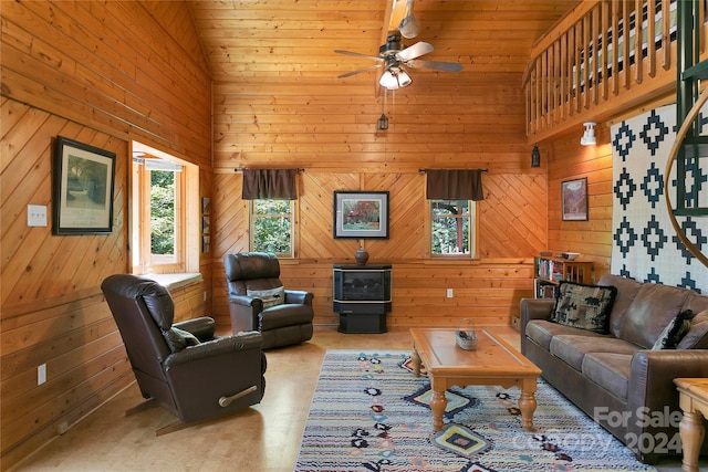 living room featuring wooden walls, a wood stove, high vaulted ceiling, light carpet, and ceiling fan